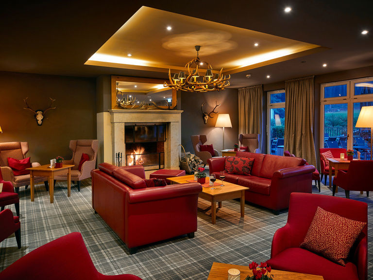 Lounge in gemütlicher Wohnzimmeroptik mit mehreren Sesseln und Doppelsitzern.